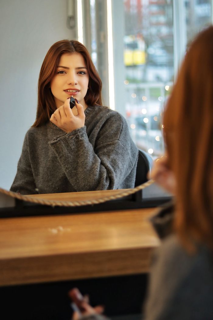 Woman applying lipstick in front of a mirror indoors. Cityscape view.